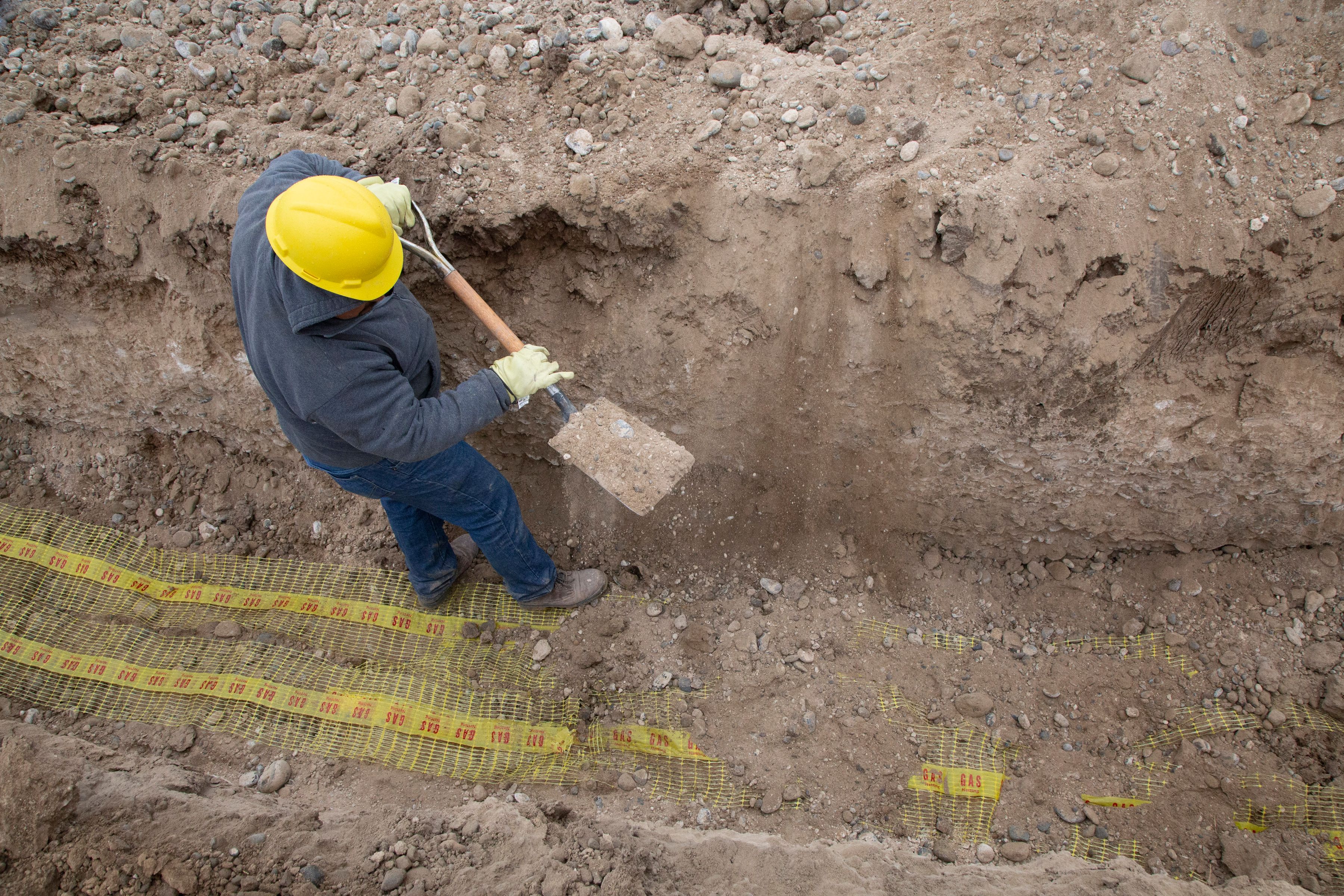 Crew member digging a utility trench by hand near marked gas lines