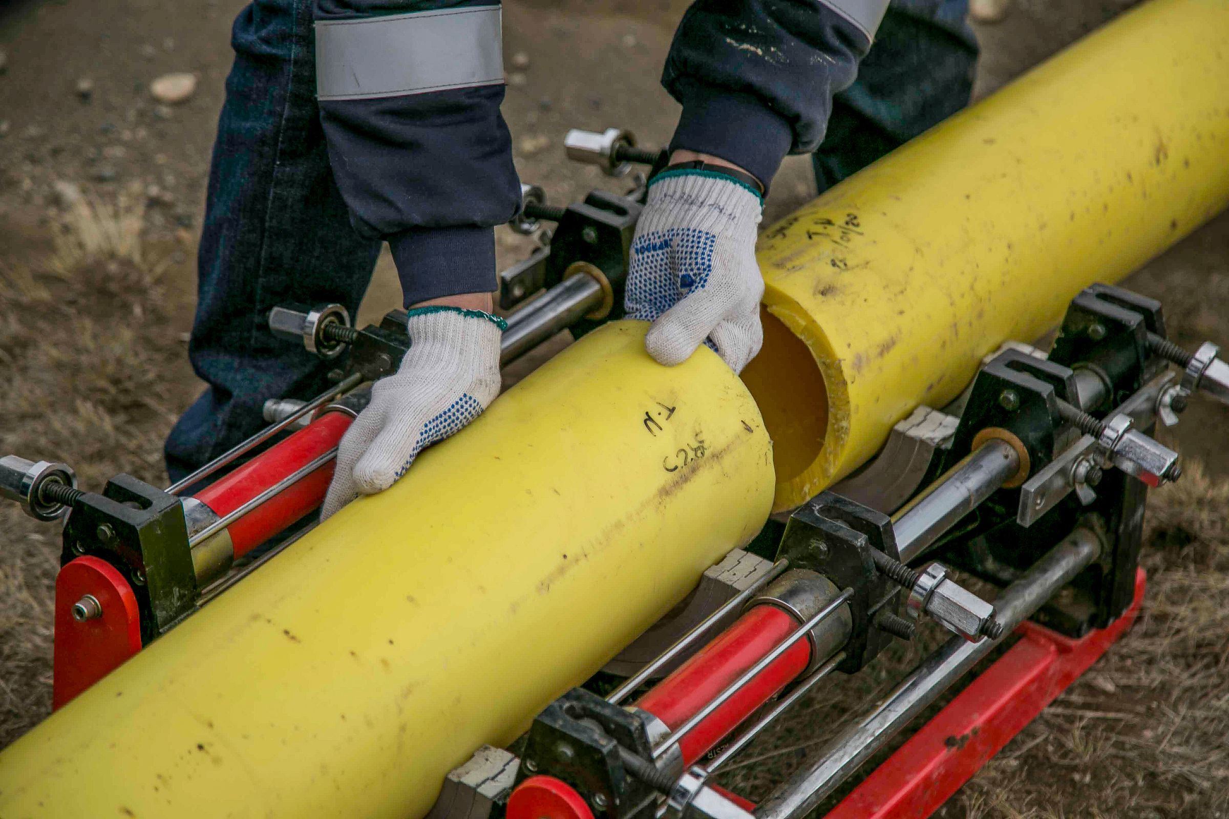 Worker's hands installing yellow utility piping outdoors